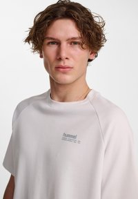 Ljusgrå kortärmad t-shirt med en liten logotyp på bröstet, i en avslappnad passform och mjukt textilmaterial.