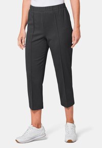 Schwarze, cropped Hosen mit einem strukturierten Stoff, ausgestattet mit einem dehnbaren Bund und vorderen Falten. Kombiniert mit weißen Sportschuhen.
