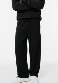 Schwarze Sweatpants aus weichem Stoff, mit lässigem Schnitt, Gummizugbund und seitlichen Taschen. Kombiniert mit weißen Sportschuhen.