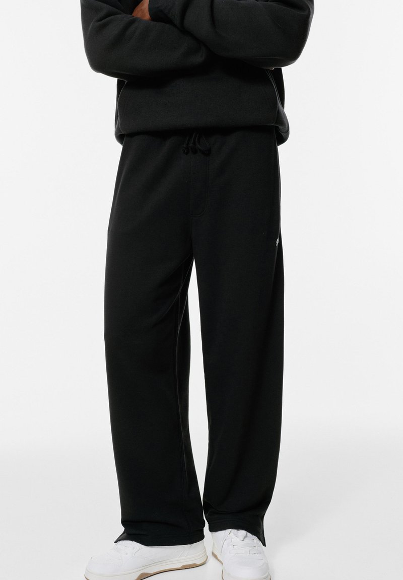 Schwarze Sweatpants aus weichem Stoff, mit lässigem Schnitt, Gummizugbund und seitlichen Taschen. Kombiniert mit weißen Sportschuhen.