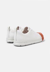 Zapatillas de cuero blanco con un acabado texturizado, punta redondeada de color naranja y forro suave en color beige. Presenta una suela de goma blanca y tiradores.