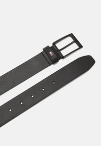 Cintura in pelle nera con fibbia rettangolare in metallo nero, con un accento del logo vicino alla fibbia e diverse perforazioni per la regolazione.