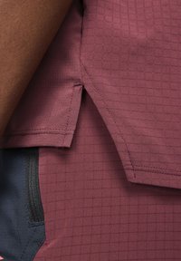 Tejido burdeos que absorbe la humedad con un patrón en cuadrícula, que presenta un bolsillo lateral con cremallera visible y dobladillo cosido para mayor durabilidad.