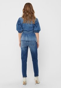 Denim jacket with puffed sleeves and a fitted waist, paired with high-waisted jeans. Light blue color with subtle fading and distressed accents.