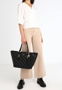 Black faux leather tote bag with quilted design, two top handles, and gold-tone hardware. Includes a tassel detail and structured shape.