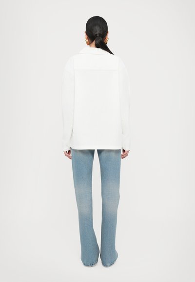 Chaqueta blanca de gran tamaño con un ligero brillo, con un cuello y hombros caídos, combinada con jeans de campana de color azul claro con un acabado descolorido.