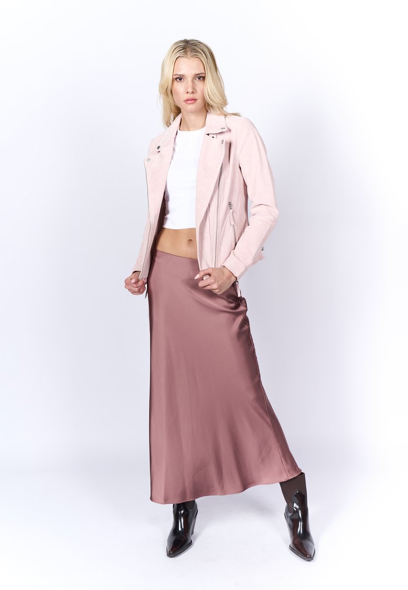Veste de motard en suède rose clair, top court blanc et longue jupe en satin marron. Bottines noires à talons aiguilles avec finition brillante et design structuré.