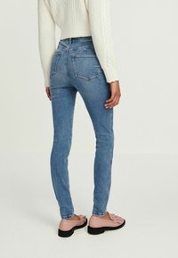 Slim fit kék farmernadrág jól kialakított derékkal és hátsó zsebekkel, rózsaszín lófaszcipővel és textúrált fehér kötött pulóverrel párosítva.
