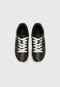 Schwarze Ledersneaker mit weißen Schnürsenkeln, die an den Seiten ein strukturiertes Streifenmuster und eine kontrastierende weiße Gummisohle aufweisen.