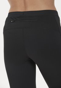 Leggings sportivi neri con un design aderente, superficie liscia e una piccola tasca con cerniera posizionata sul retro per lo stoccaggio.