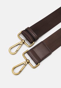 Cinghia in tessuto marrone con accenti in pelle, dotata di due clip metalliche dorate e una superficie testurizzata, progettata per un attacco sicuro.