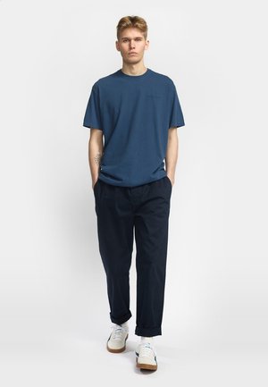 Blauwe katoenen T-shirt met een ronde halslijn, korte mouwen en een subtiele logo. Gecombineerd met donkerblauwe broek en witte sneakers.