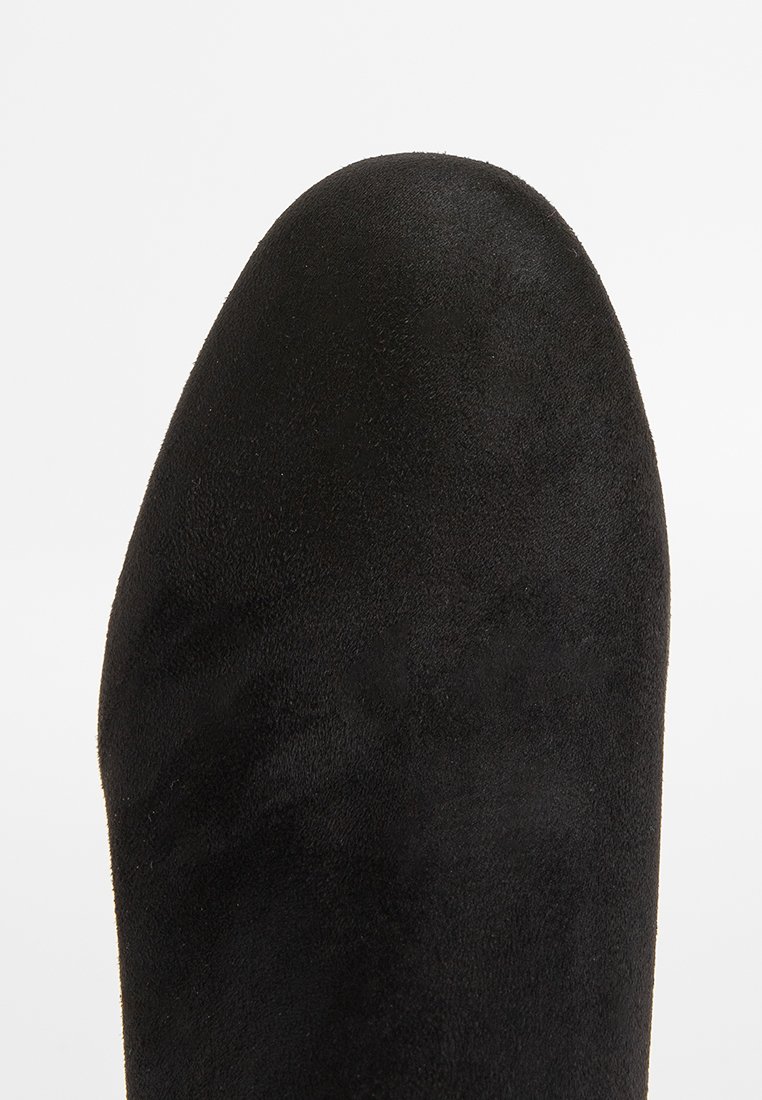 Bottine noire en suède avec un bout arrondi, texture lisse et design minimaliste. Pas de quincaillerie ni de motifs visibles.