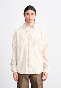 Cremefarbenes Button-Up-Hemd mit dünnen roten vertikalen Streifen, langen Ärmeln und einer Brusttasche. Aus einem weichen, strukturierten Stoff gefertigt.