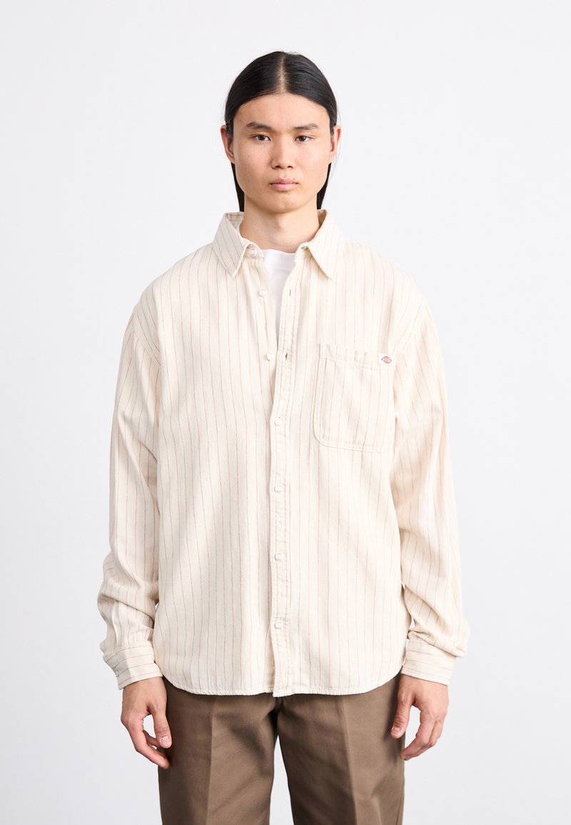 Cremefarbenes Button-Up-Hemd mit dünnen roten vertikalen Streifen, langen Ärmeln und einer Brusttasche. Aus einem weichen, strukturierten Stoff gefertigt.