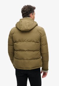 Chaqueta de plumas sólida color verde oliva con capucha, que presenta un diseño acolchado horizontal, puños elásticos y un logo en la parte posterior.