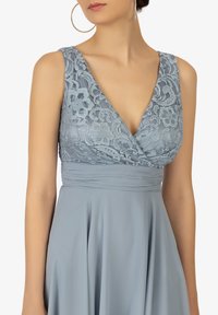 Abito azzurro chiaro con corpetto in pizzo, scollatura profonda e vita arricciata. Il tessuto fluente crea una silhouette elegante e morbida.