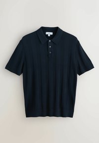 Tumesinist värvi lühikeste varrukatega polosärk, millel on tekstureeritud vertikaalsed triibud, kolme-nupuline plastron ning soonikservad ja mansetid.