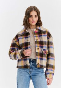 Flanelová bunda s vícebarevným kostkovaným vzorem v béžové, modré, růžové a hnědé barvě. Má zapínání na knoflíky vpředu a kapsu s růžovým akcentem.
