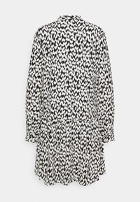 Svartvit mönstrad klänning med krage, lång ärm och utsvängd nederdel. Tillverkad av lätt material med en texturerad yta.