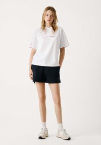 Camiseta de algodón blanca con el texto "RED BULL RACING" en rojo, combinada con pantalones cortos negros, calcetas blancas y zapatillas ligeras.