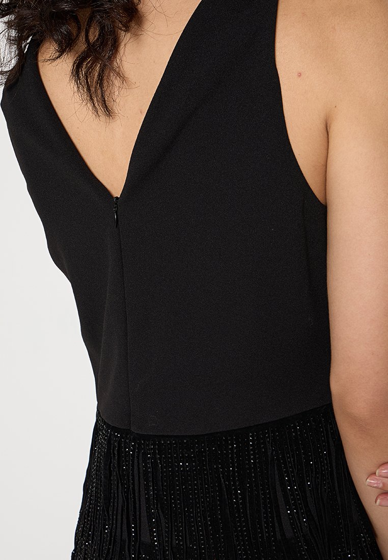 Czarna sukienka z głębokim dekoltem z tyłu, gładkiego materiału i frędzlami z detalami z koralików, tworząca teksturalne zainteresowanie wizualne.