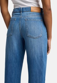 Jeans in denim blu a vita alta con vestibilità dritta, dotati di un'etichetta in pelle sul retro e due tasche posteriori.