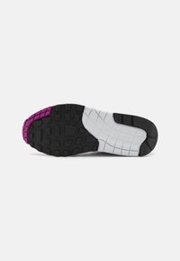 Podplat čevlja z črnim, belim in vijoličnim gumijastim profilom, ki vsebuje kvadratne in pravokotne oprijemalne površine ter odtisnjen napis "NIKE AIR" na belem delu.