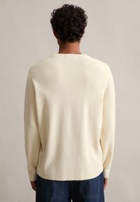 Kremowy sweter dzianinowy o luźnym kroju, z prążkowaną teksturą, okrągłym dekoltem i opadającymi ramionami. W połączeniu z ciemnymi dżinsami.