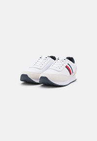 Sneakers bianchi con tomaia in pelle liscia, accenti in suede, tallone blu navy e strisce rosse e blu navy. Suola in gomma spessa con grip testurizzato.