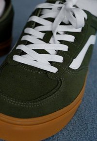 Grøn ruskinds sneakers med hvide snørebånd og striber, gummisål, med perforeringer på tåen og teksturerede sideakkenter.