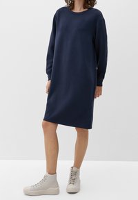 Mörkblå sweatshirtklänning med långa ärmar, rund halsringning och sidokliv, kombinerad med ljusgrå hög-top sneakers. Slät tygtextur.