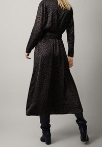 Robe longue et sombre avec un motif léopard, taille cintrée et tissu fluide. Assortie à des bottes noires jusqu'aux genoux.