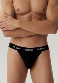 Czarny stringi wykonane z elastycznego materiału, z czarną talią i białym napisem "ATLANTIC". Minimalistyczny design, gładka tekstura.
