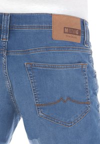 Jeans in denim blu con una toppa in pelle marchiata "MUSTANG True Denim", con cuciture arancioni a contrasto e un design classico delle tasche.