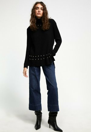 Black ribbed turtleneck sweater with metallic studs at the hem, paired with wide-leg denim jeans and black pointed ankle boots.