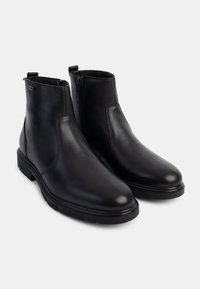 Botas de piel negra hasta el tobillo con un acabado suave, cierre de cremallera lateral y suela de goma resistente. Diseño minimalista sin patrones visibles.