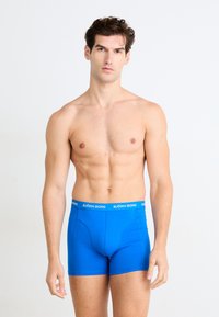 Boxers bleus en tissu extensible, avec une ceinture noire comportant le logo "BJÖRN BORG" en blanc. La coupe est ajustée et sans coutures.