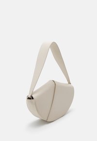 Borsa a spalla in pelle beige con design curvo, dotata di una larga tracolla e di un distintivo sistema di chiusura a patta piegata. Texture liscia e hardware minimal.