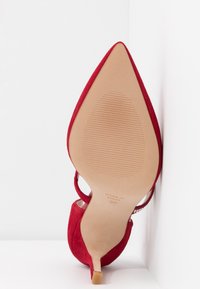 Chaussure à talon haut pointu en suède rouge vue de la semelle, avec un talon fin et la mention "Made in Spain 37" estampillée en bas.