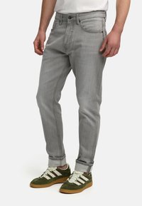 Lysegrå denimjeans med en tætsiddende design, der har klassisk fem-lomme stil og opkørte manchetter. Båret med grønne og hvide sneakers.