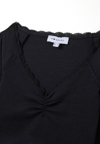 Schwarzes Oberteil mit V-Ausschnitt, gerafftem Zentrum und gewelltem Spitzenbesatz. Hergestellt aus weichem Material mit glatter Textur. Das Etikett zeigt die Größe S.