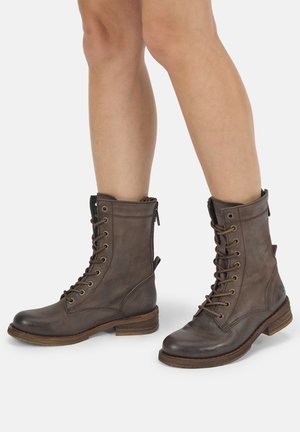Brown leather lace-up ankle boots worn on bare legs, with a low wooden heel and round toe design on a white background.