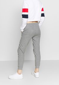 Grå joggerbyxor med smalnande ben och elastisk midja, tillsammans med en vit kortärmad sweatshirt med röda och marinblå ränder på ärmarna.