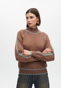 Hnědý pletený svetr s vysokým límcem, zdobený tyrkysovými akcentními pruhy na ramenou a manžetách. Měkká textura, volný střih.