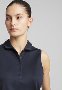 Bezrukávový polo tričko v námorníckej modrej farbe s golierom a zapínaním na gombíky. Tkanina má hladkú, mierne lesklú štruktúru.