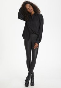 Schwarzes Button-Down-Hemd mit langen Ärmeln, kombiniert mit eng anliegenden schwarzen Hosen und schwarzen Stiefeletten mit hohen Absätzen. Glatte Textur und elegantes Design.