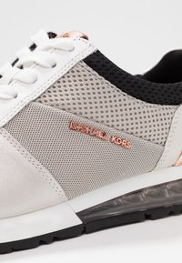 Białe i szare sneakersy z siateczkowymi panelami, czarnymi akcentami i różowo-złotym logo. Posiadają teksturowaną skórę, gumową podeszwę oraz wiązany design.