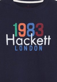 Námořnické tričko, bavlněný materiál, se zajímavým textem: "1983 Hackett London" v červené, oranžové, zelené, modré a bílé barvě. Kulatý výstřih, krátké rukávy.