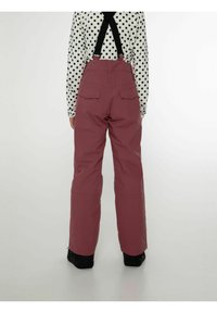 Vaaleanpunaiset lumihousut, joissa on säädettävät mustatolkaimet, kaksi takataskua ja väljä malli, käytetty mustavalkoisen pilkullisen paidan päällä.